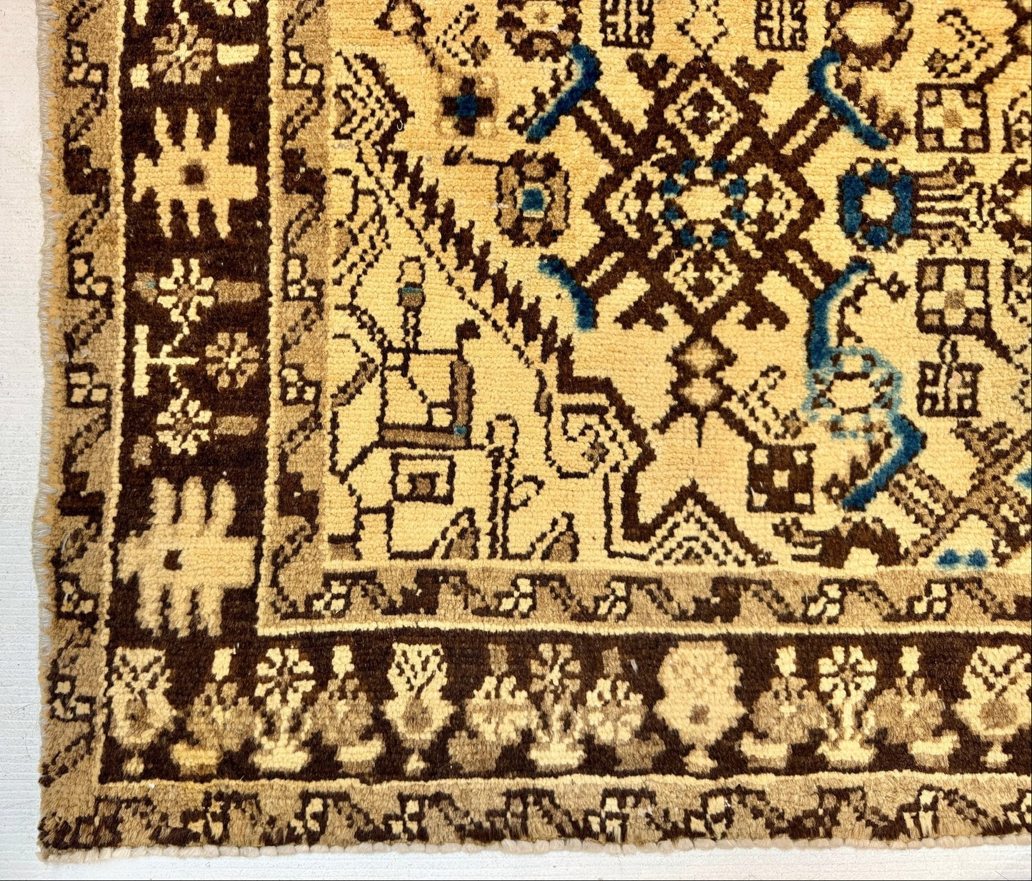 Close-up of a patterned area rug corner showing a cream and dark brown field with a decorative border and small blue accents.