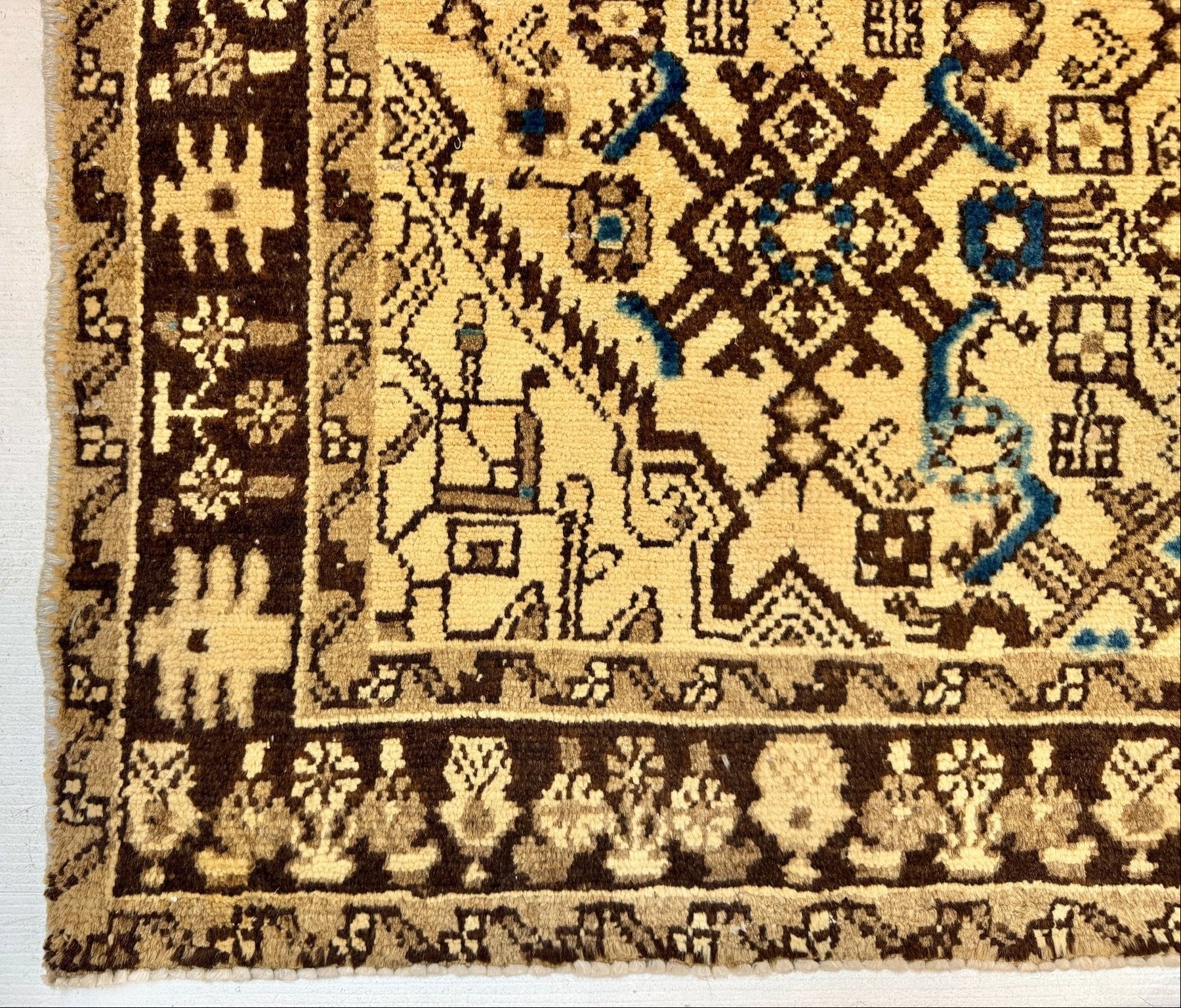 Close-up of a patterned area rug corner showing a cream and dark brown field with a decorative border and small blue accents.